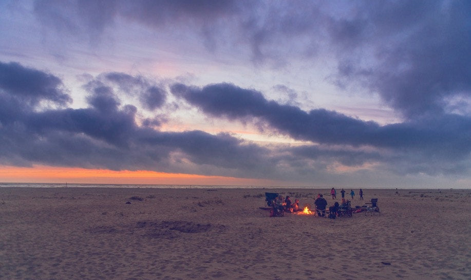 group of people on the beach around a campfire