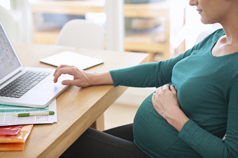 Young pregnant woman is working on laptop