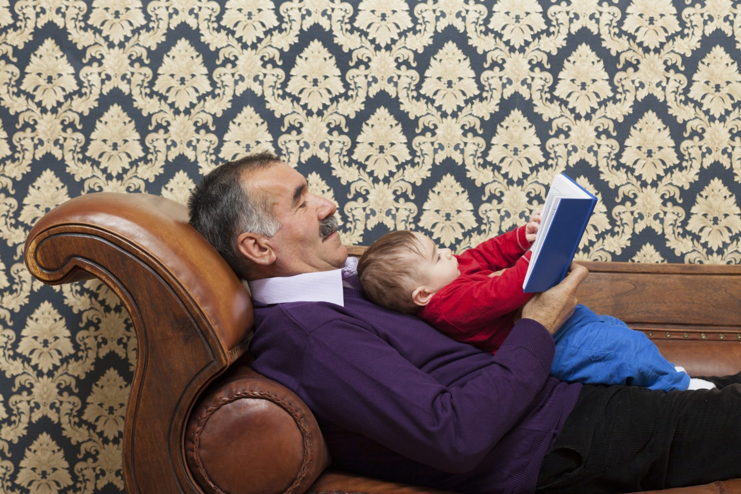 grandfather reading book for newborn grandson on a sofa