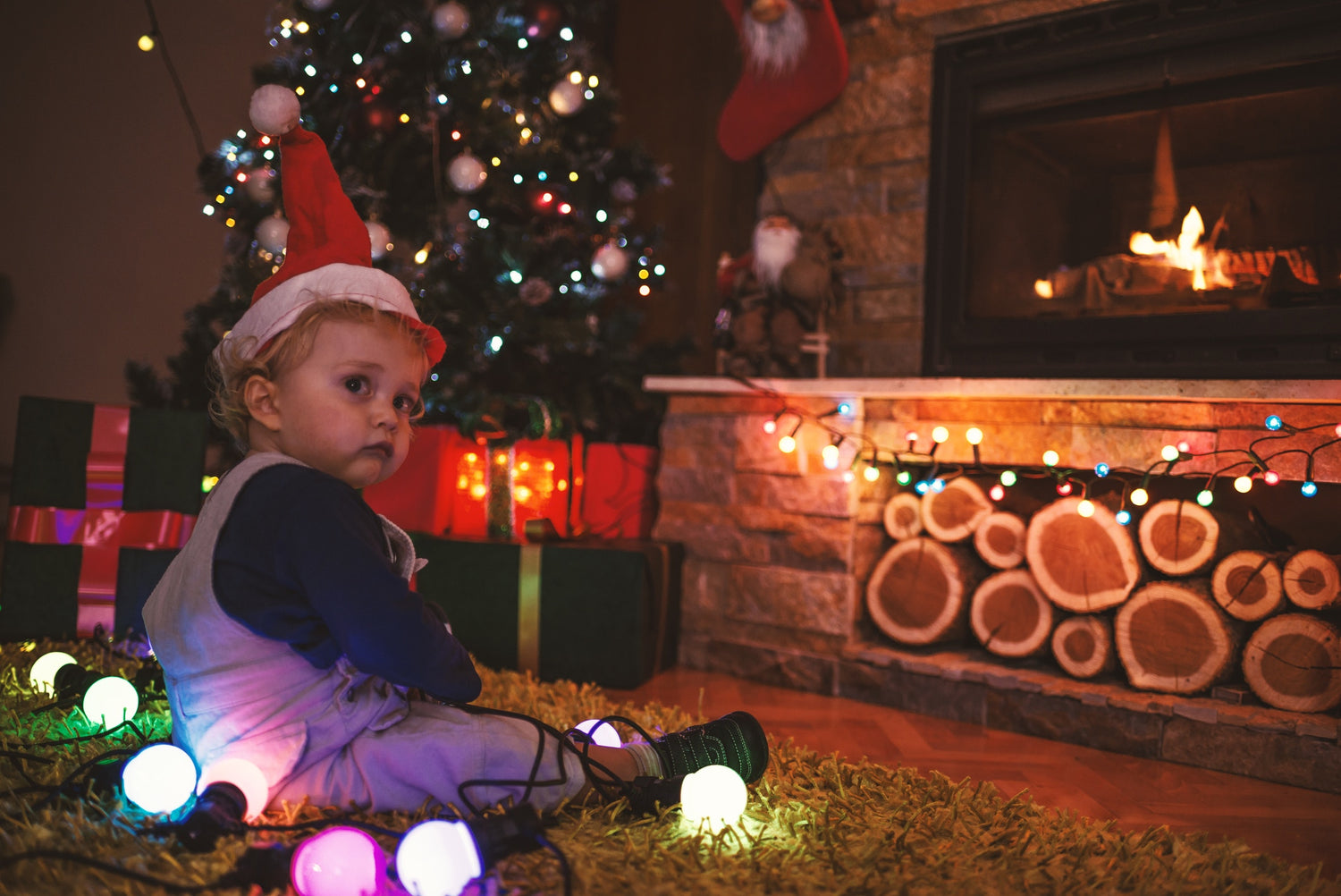 little baby boy in a Christmas cap sitting on floor by the Christmas tree
