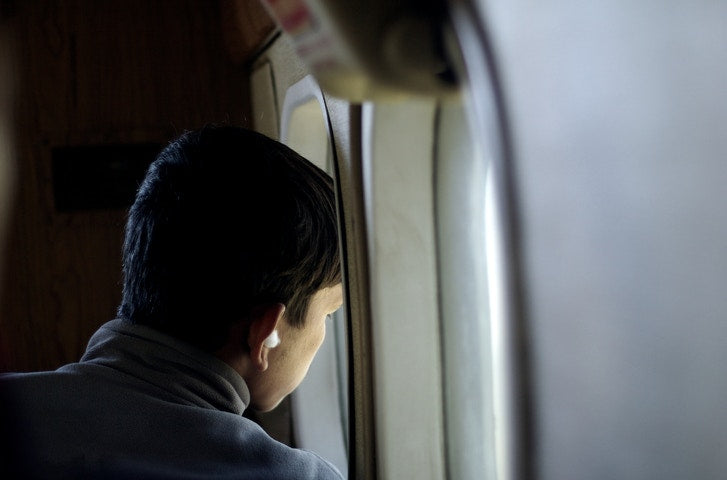 boy sitting on the seat looking out an airplane window while flying