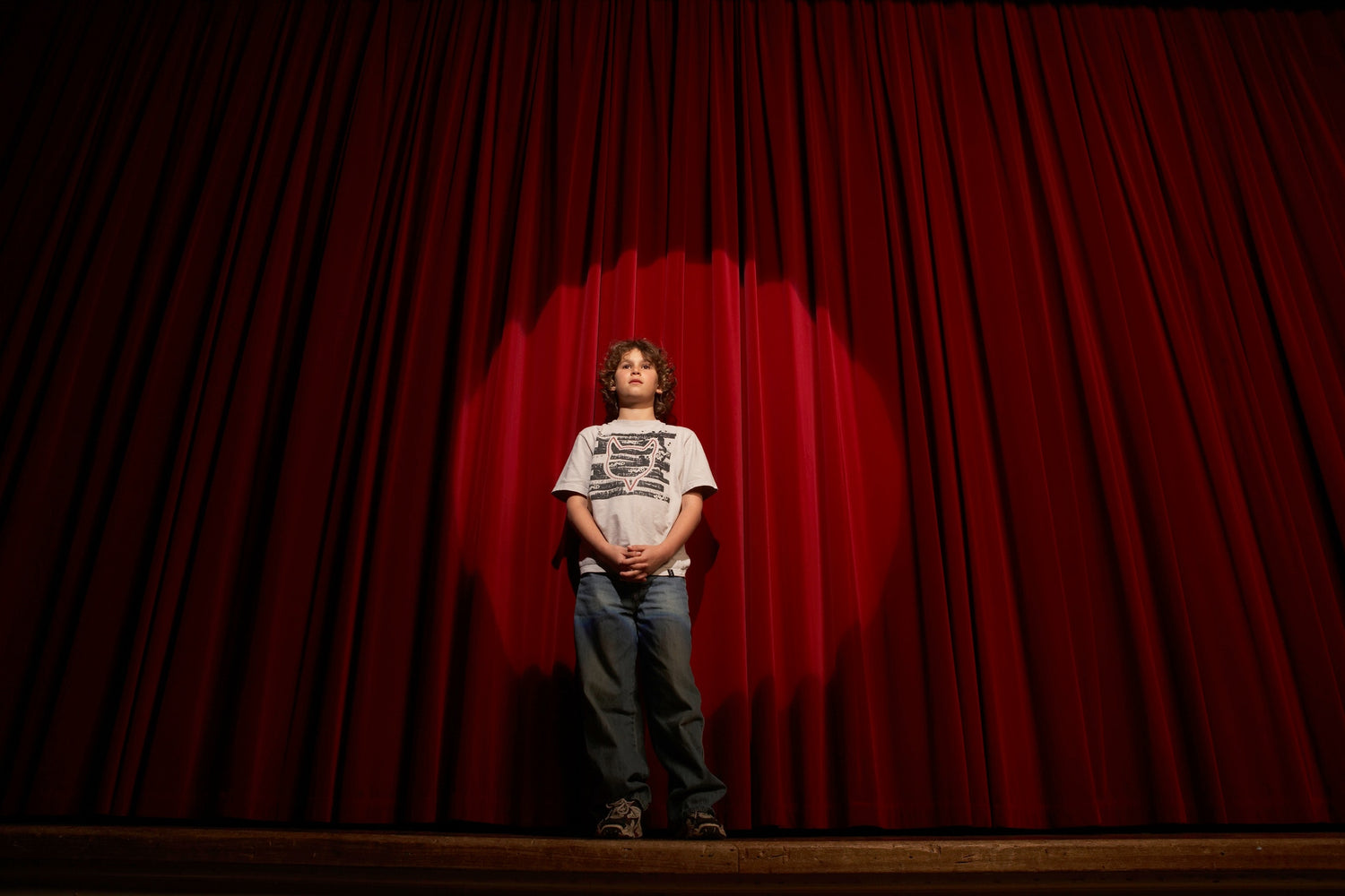 young boy performing at the stage with red curtains