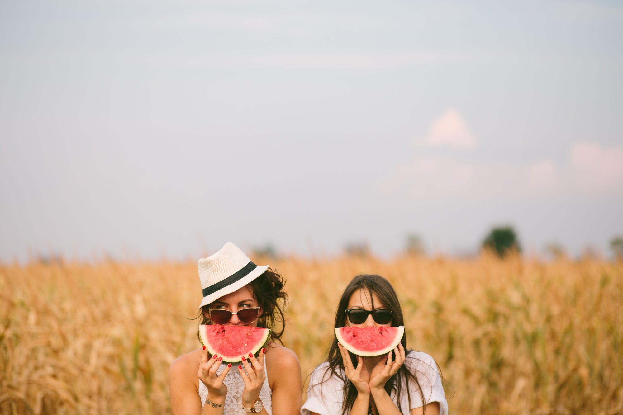 two beautiful womens covering face with watermelon in wheat field
