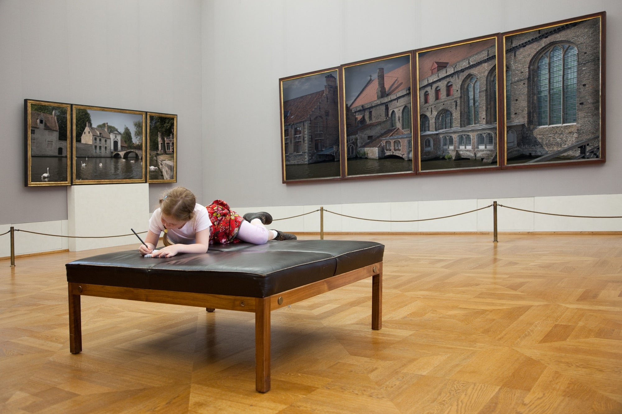 Little girl sitting on the sofa and drawing in a large exhibition room