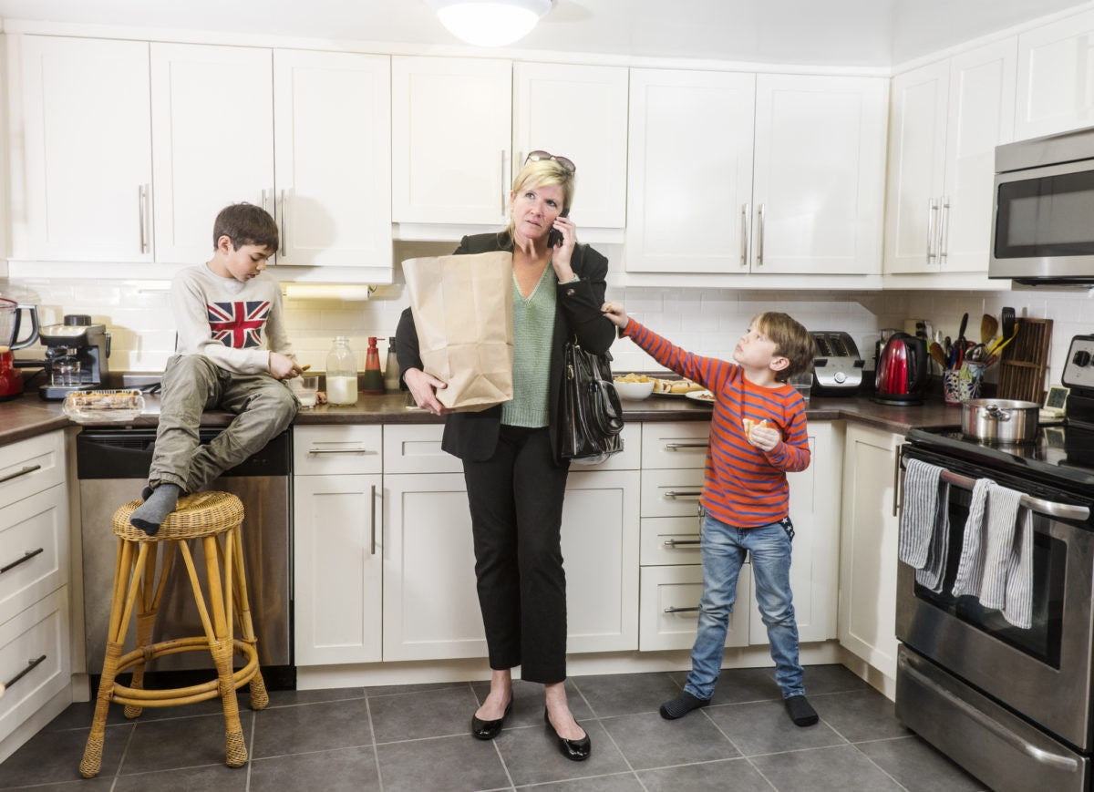 two sons with mom talking on phone and holding grocery at kitchen