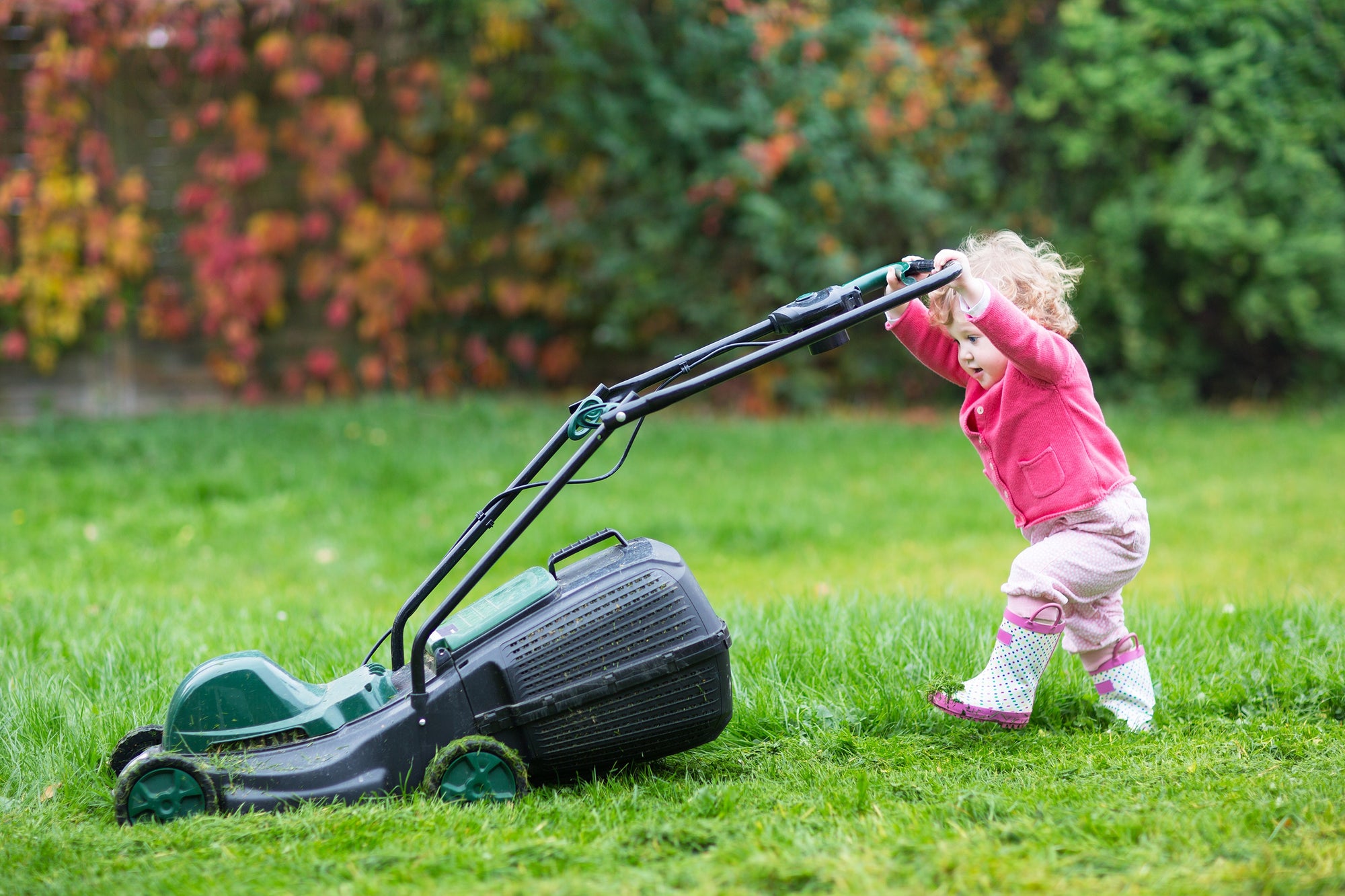 Cute curly baby girl  with big green lawn mower