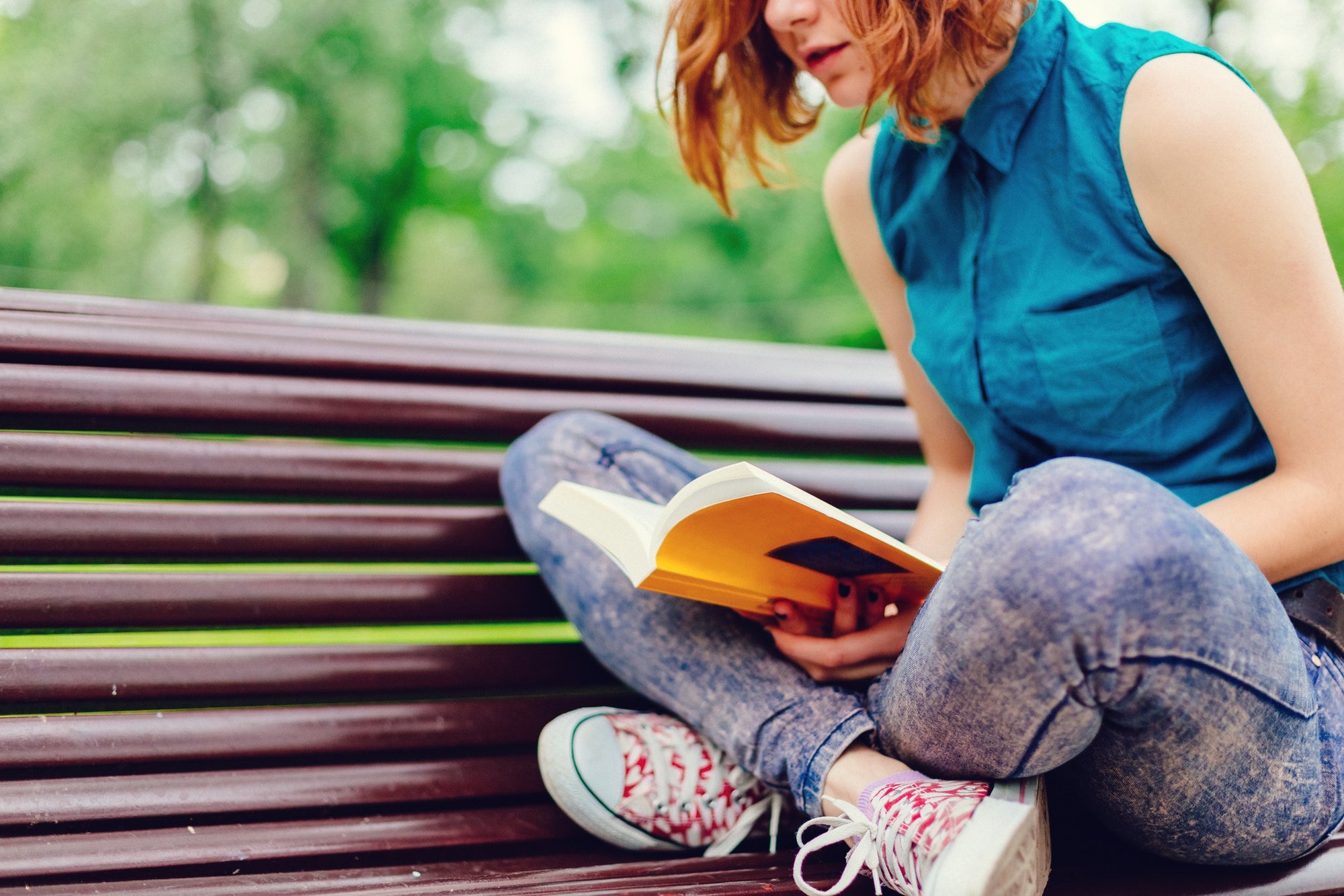 Young woman sitting on a bench in the park and reading book
