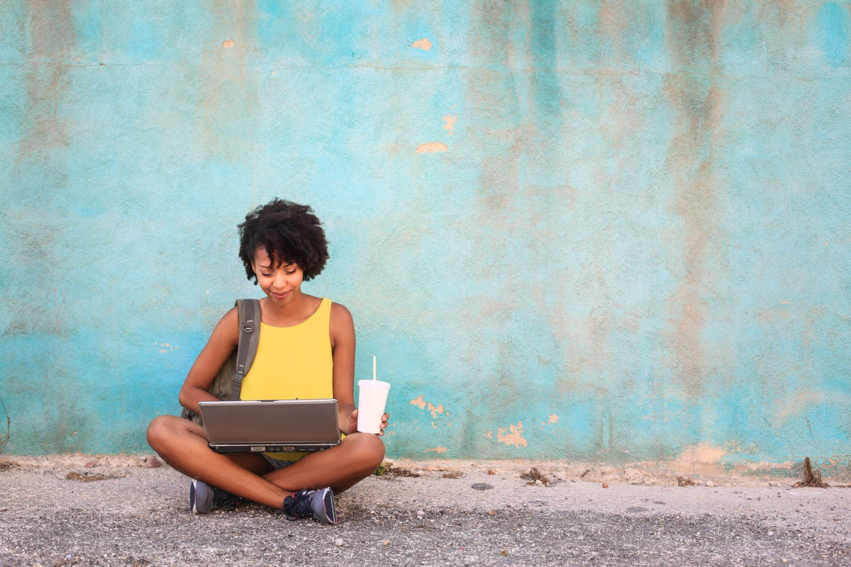 A woman sitting on the road and using laptop 