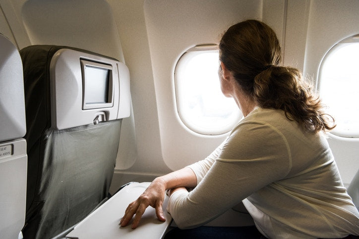 woman sitting on the seat looking out an airplane window while flying
