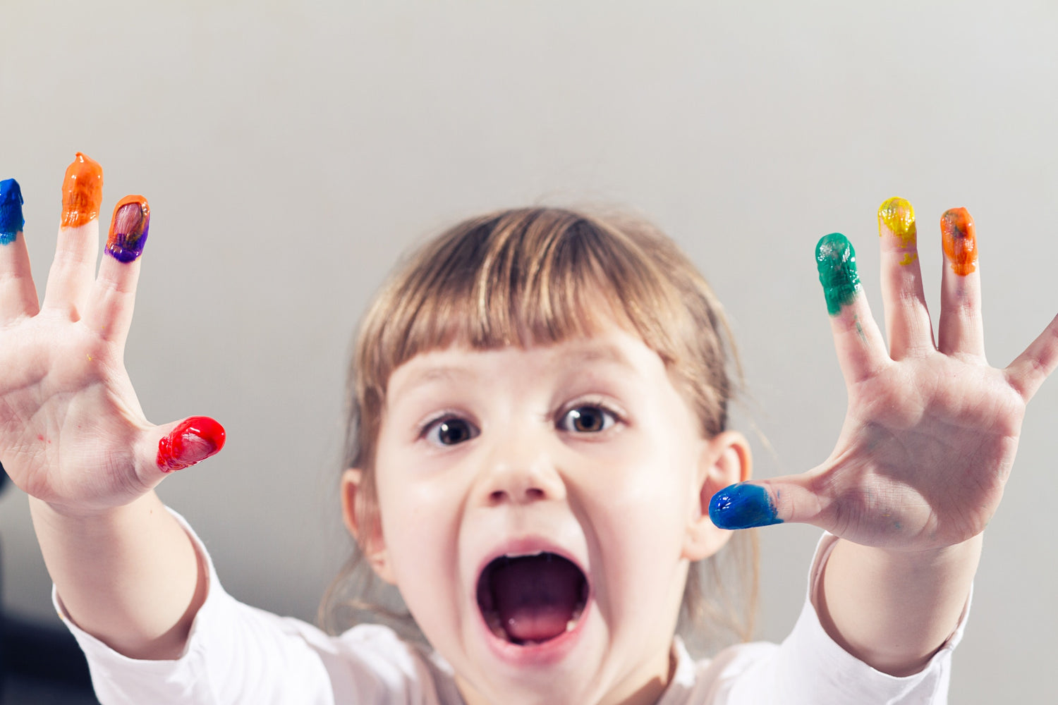 Little girl showing her hands, covered in finger paint after painting a picture