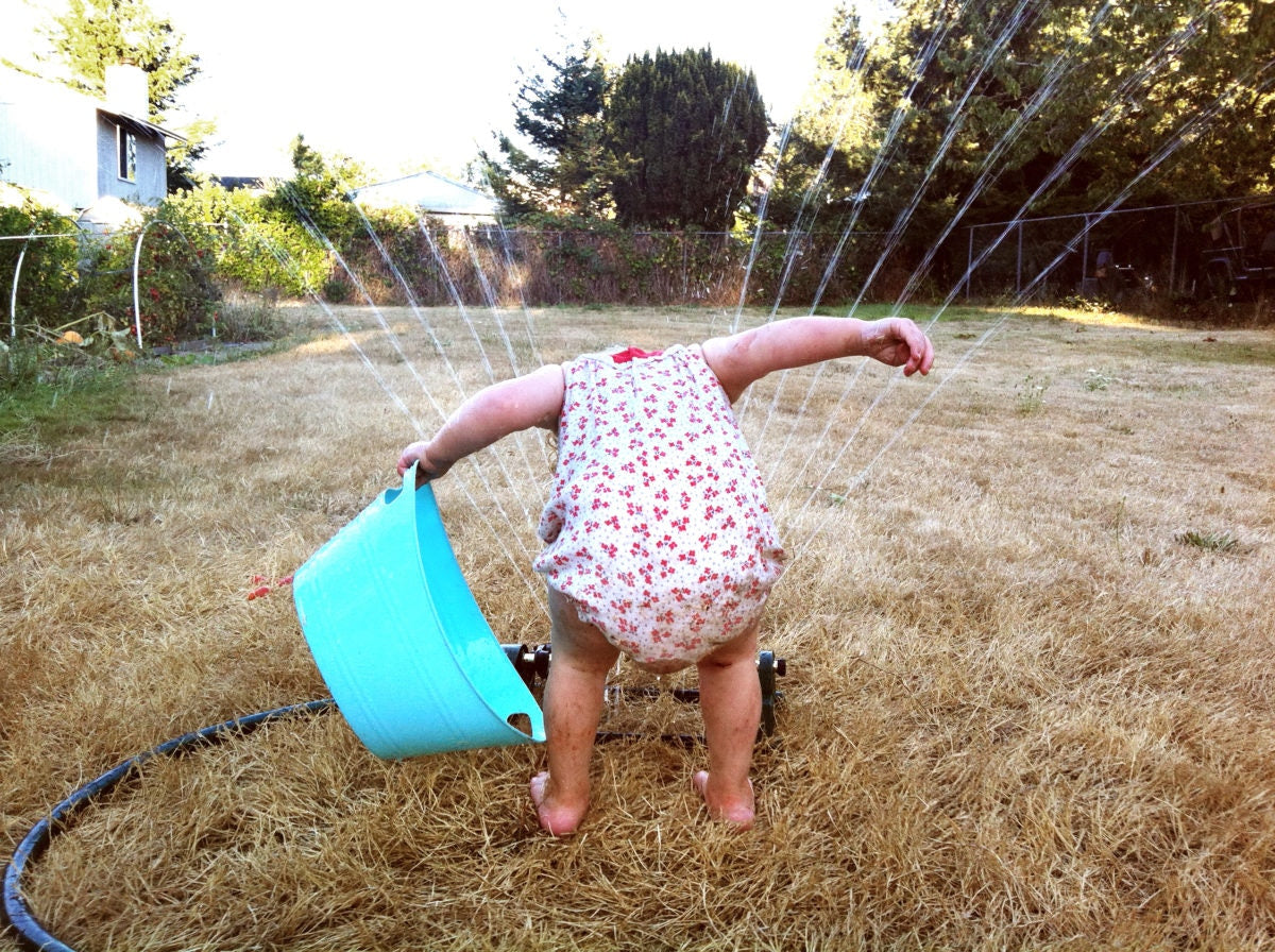 A kid is playing in a garden by sprinkling water