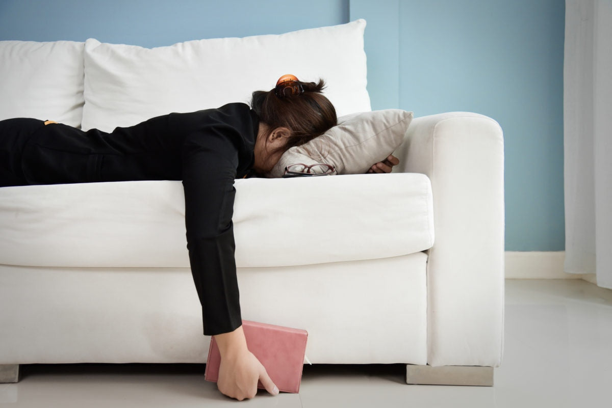 Woman lying in couch with face buried in pillow and a book in her hand