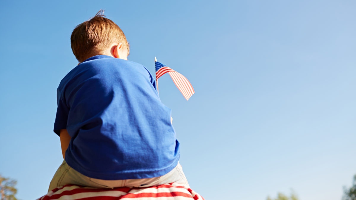 Boy sitting on a shoulder by holding US flag
