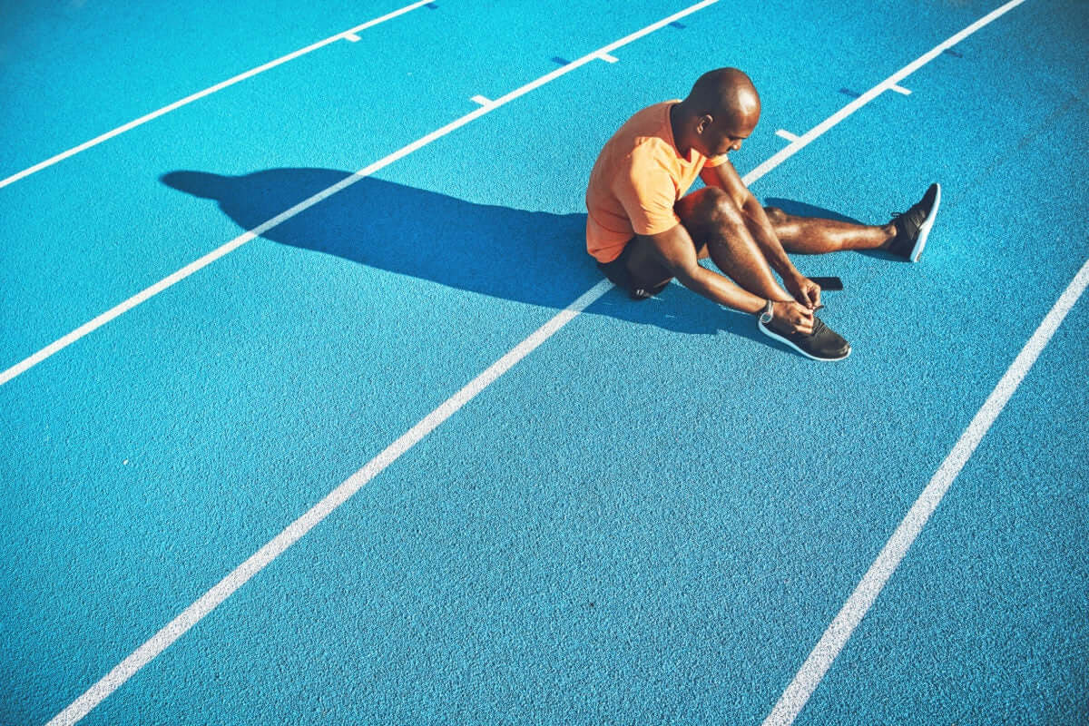 Man tightening his shoe laces sitting on the ground on a running track