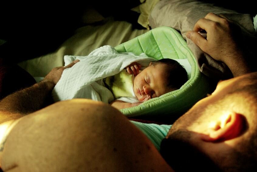 father and a baby sleeping on bed