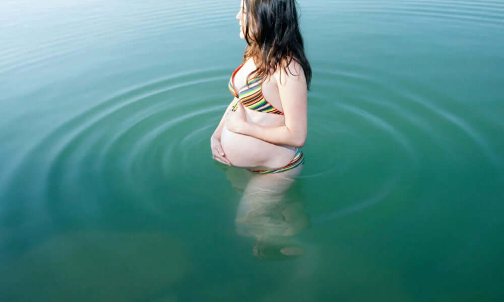 pregnant women touching her belly and standing in water