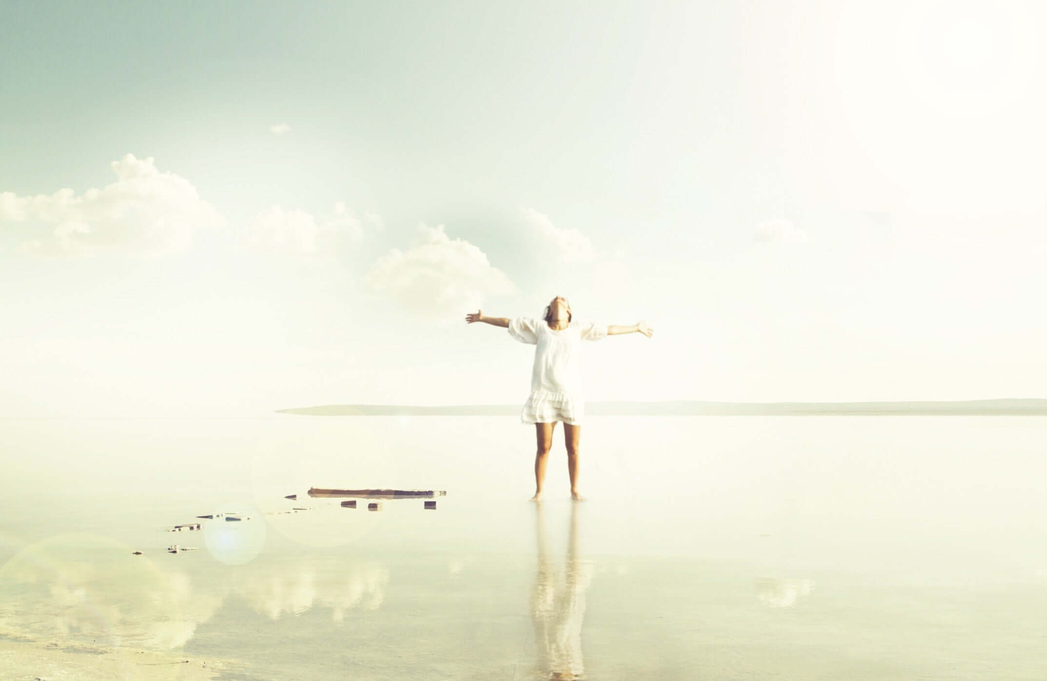 Young woman standing on the shore of scenic lake with her hands raised.