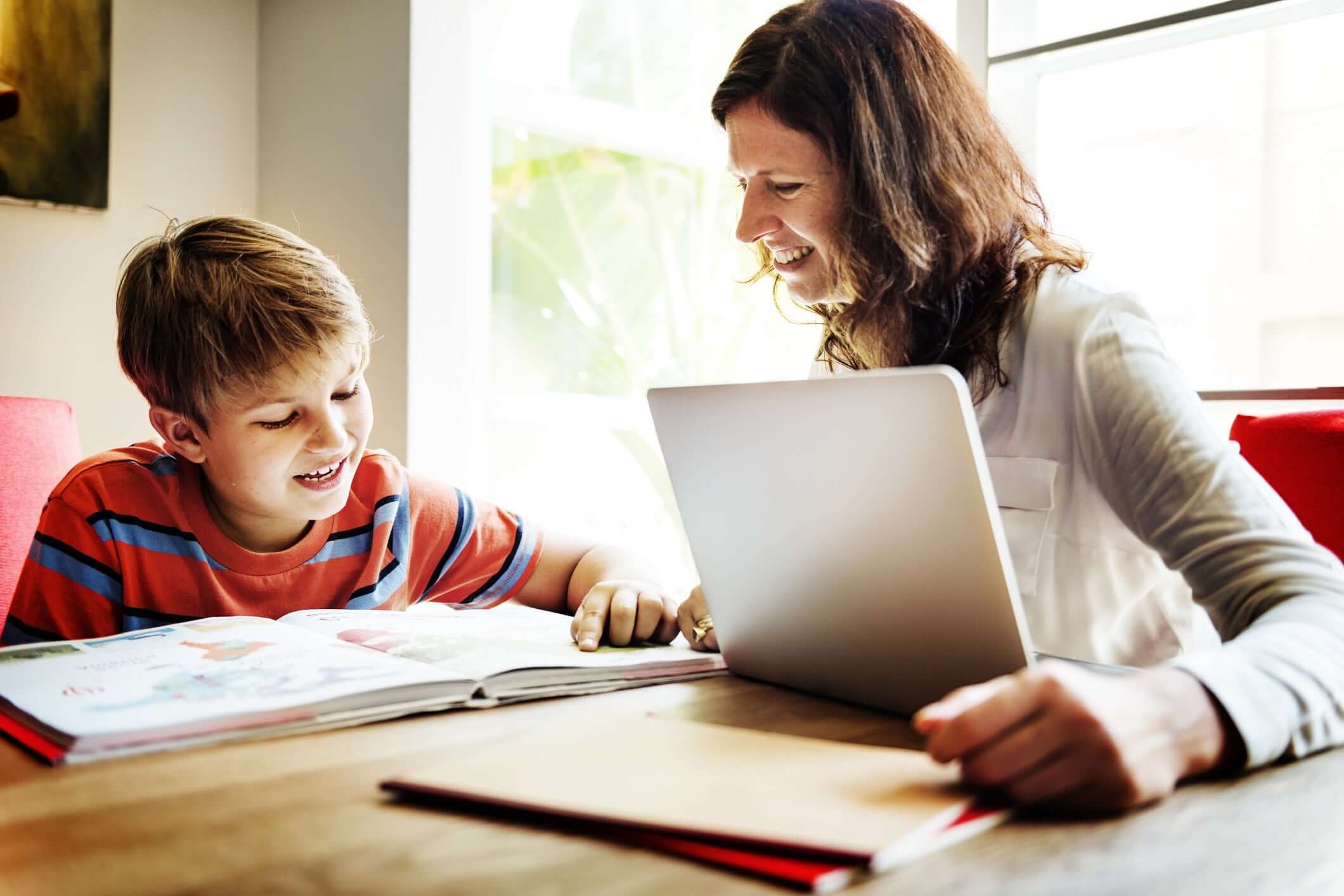 Mother helping son while he is studying and she is working on laptop at home