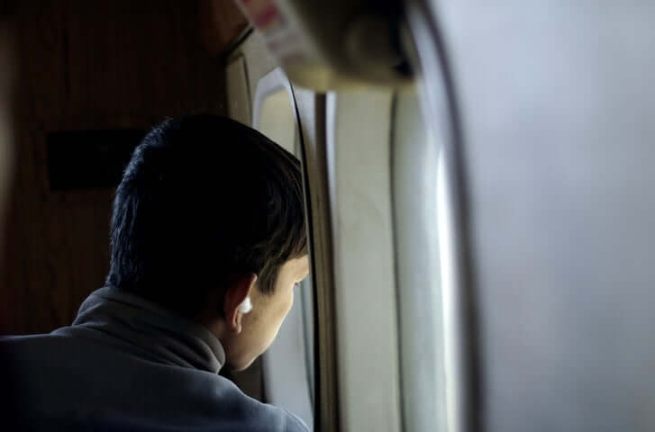 boy sitting on the seat looking out an airplane window while flying