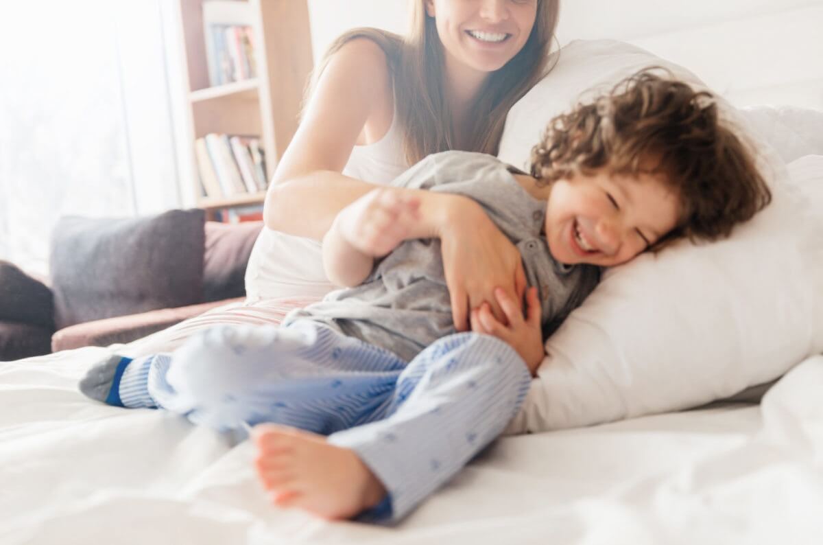 happy mother tickling her son in bed and laughing