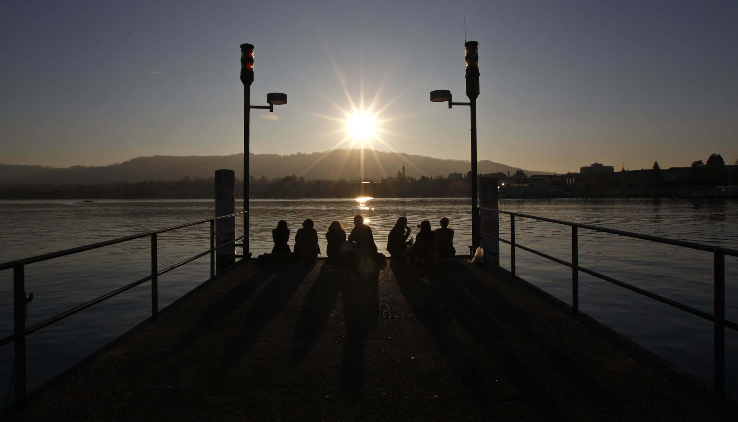 friends sitting on wooden dock during sunset