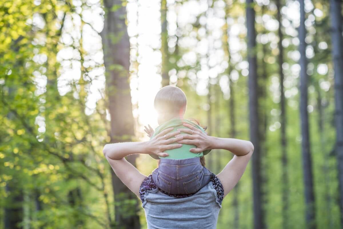 mother walking with her baby son in a beautiful nature as he sits on her shoulders
