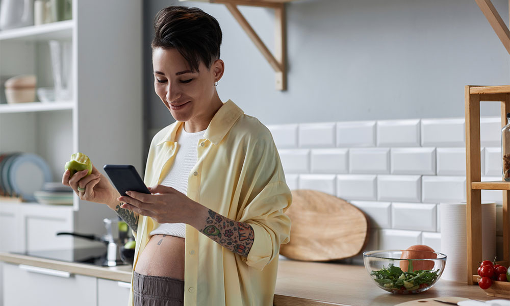 pregnant young woman holding smartphone in kitchen