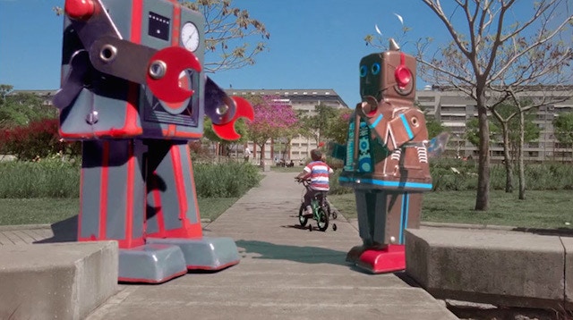large robots with a child riding a bike in-between them