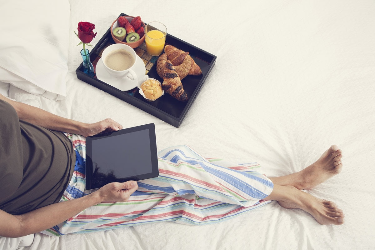 woman laying in bed with breakfast looking at a tablet