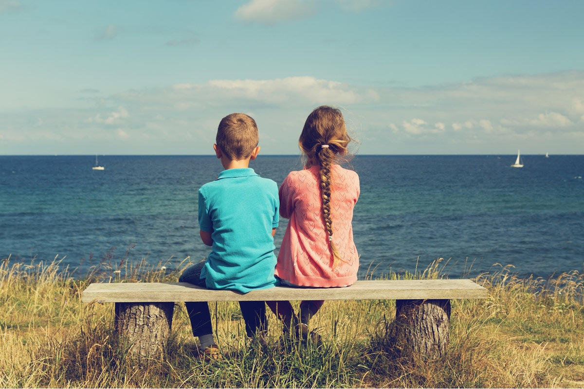 boy and girl sitting on a bench looking at the sea