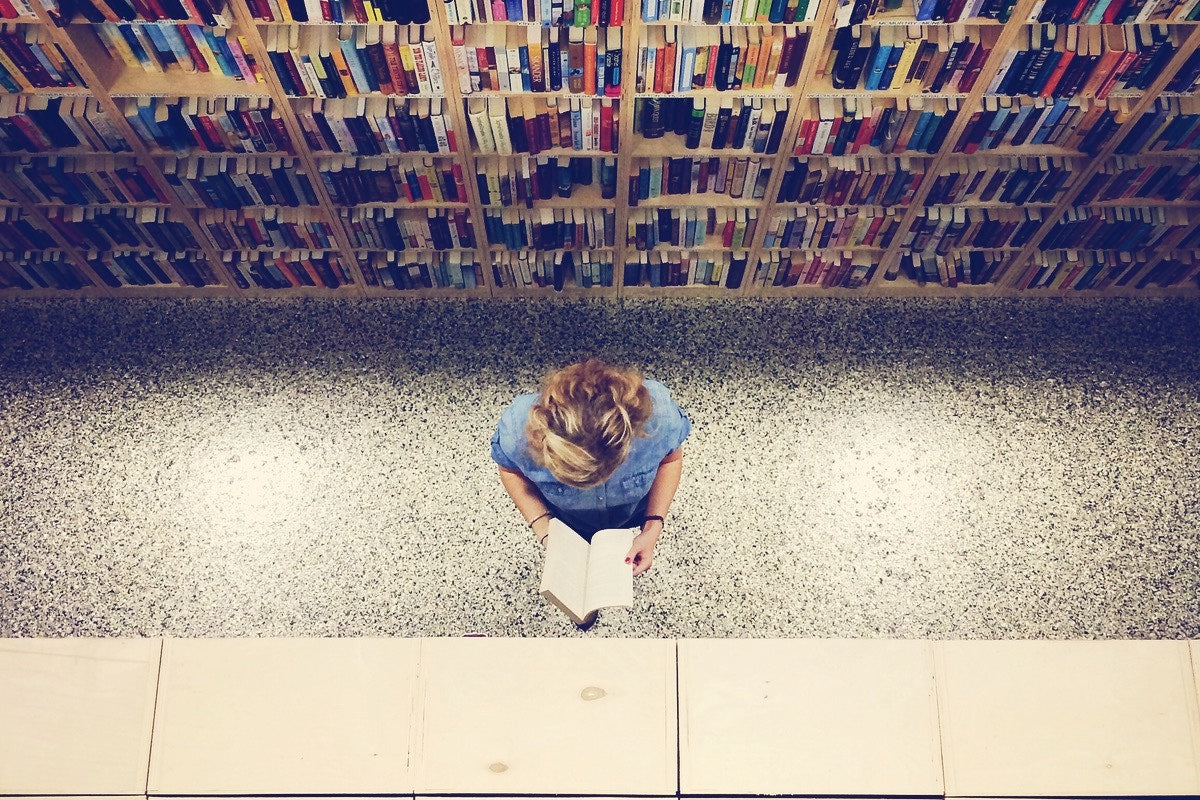 overhead shot of a woman reading a book in a library isle