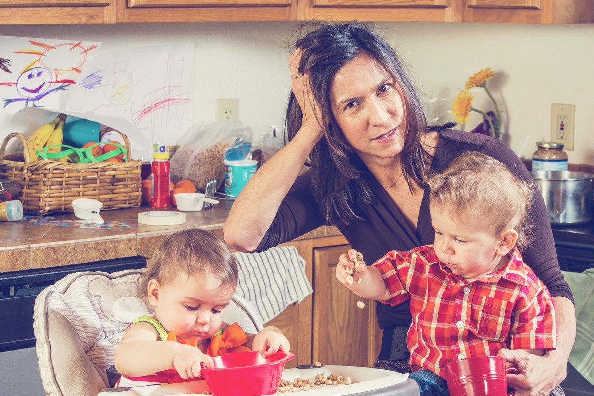 mom with two toddlers in a kitchen looking frustrated 