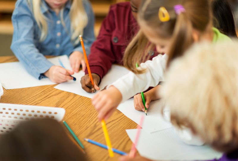 four kids around a table with pens and paper