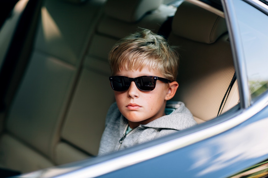 Cool little boy in sunglasses sitting in a child seat in the rear of a car