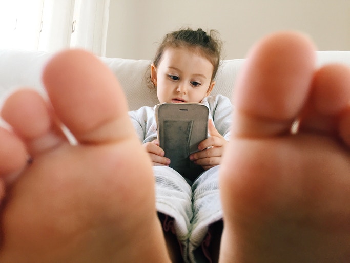 little girl  with legs stretched out on a bed using mobile phone