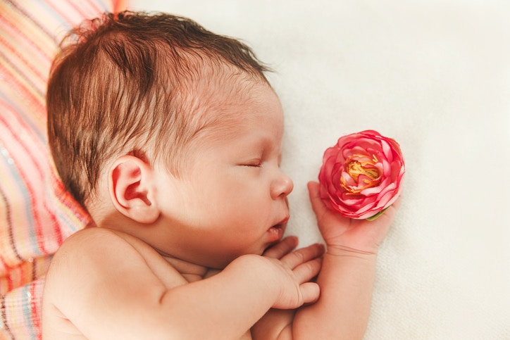cute newborn baby with flower in small touching hand