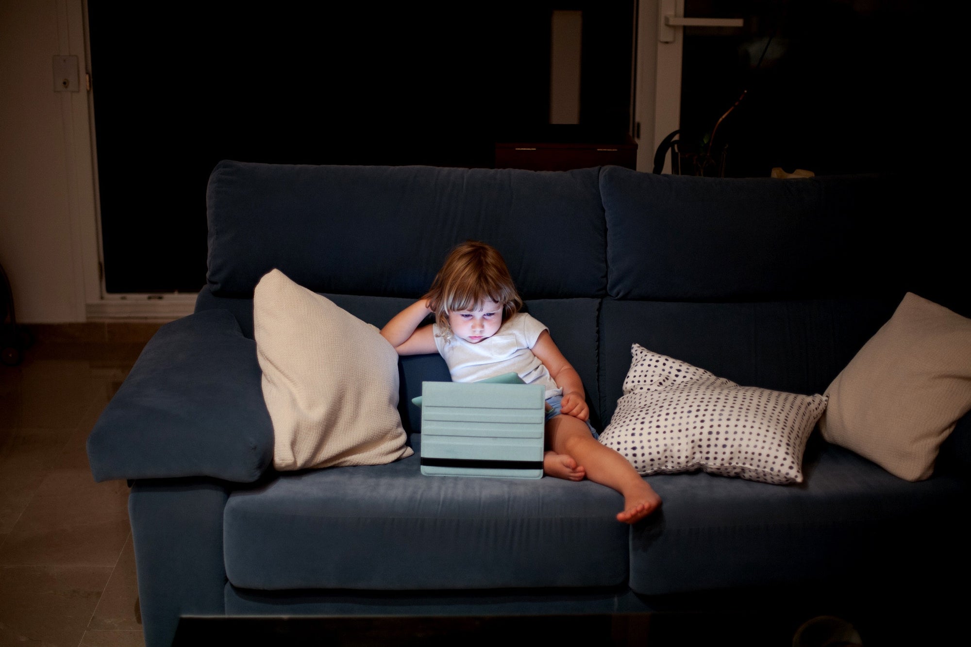 little girl sitting on sofa watching movie on tablet
