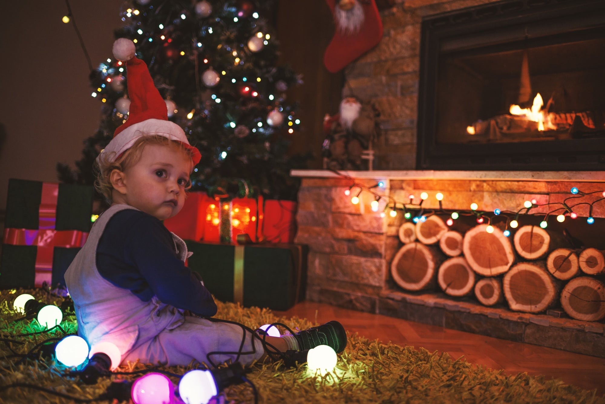 little baby boy in a Christmas cap sitting on floor by the Christmas tree