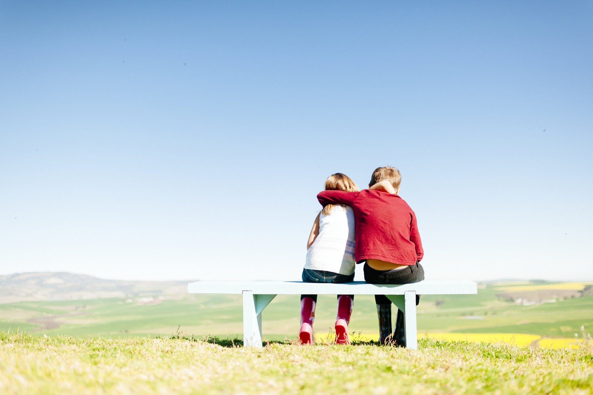 rear view of boy and girl sitting on bench at  field