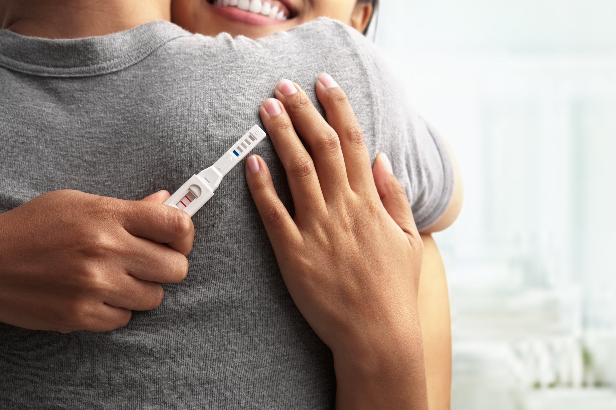 Young happy women hugging husband holding positive result pregnancy test