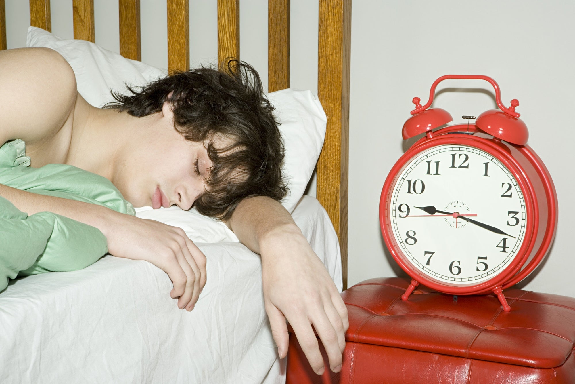 A person sleeping in a bed beside an alarm clock