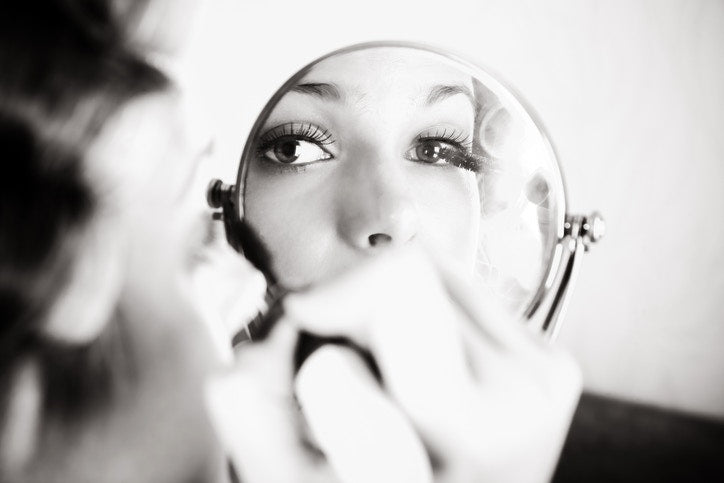 reflection of woman applying mascara on mirror