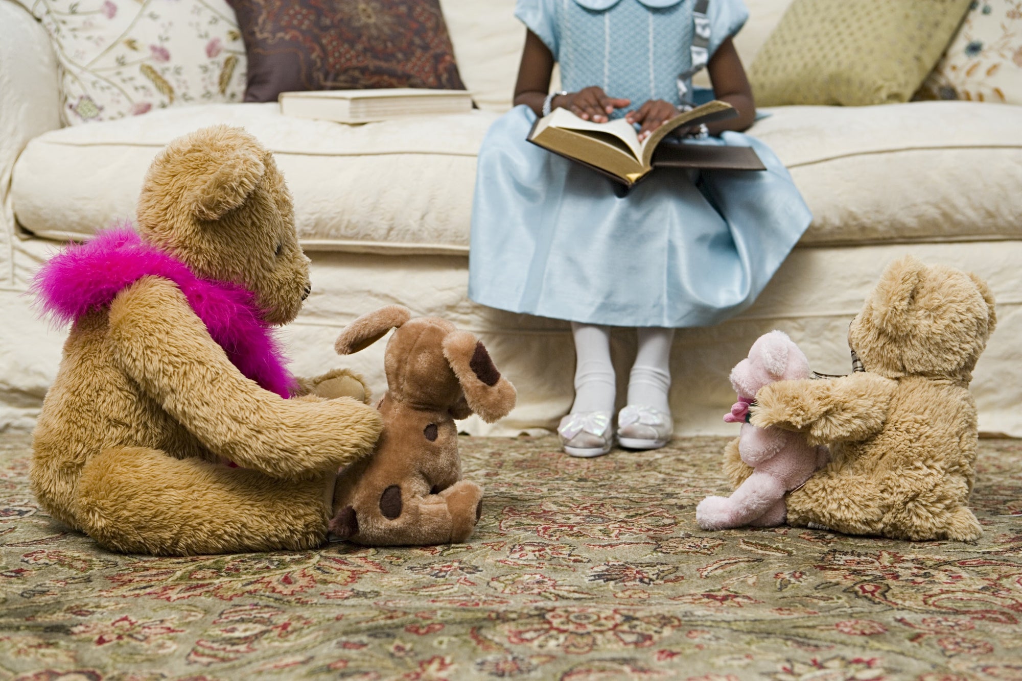 young girl sitting on sofa with book and teddy bear on floor