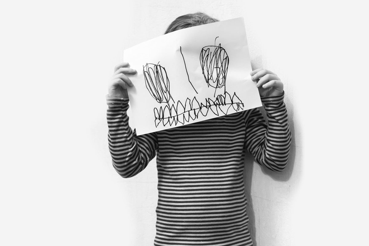 little girl cover her face  with drawing on paper