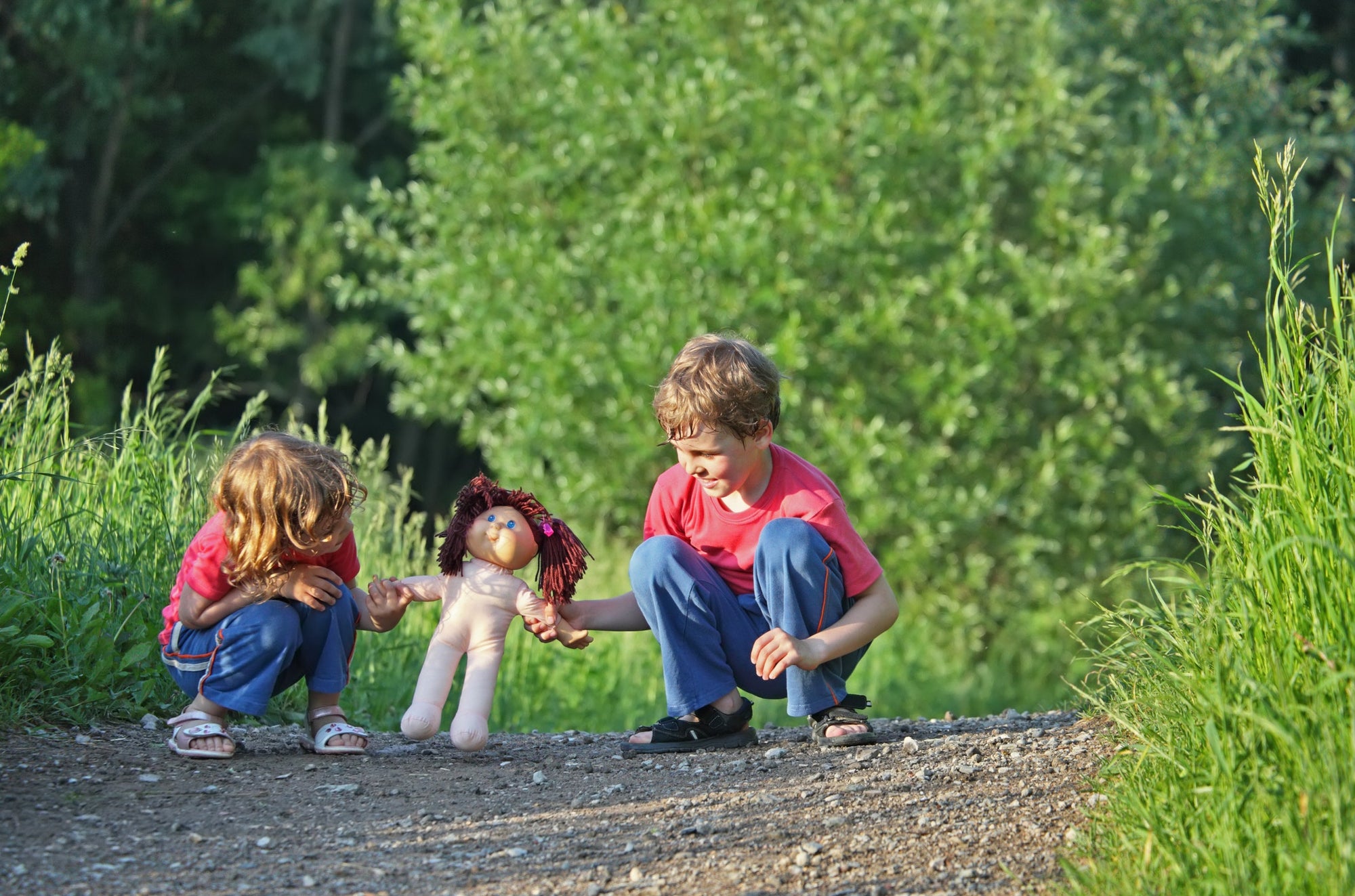 Little children boy and girl sitting on forest ground playing with doll