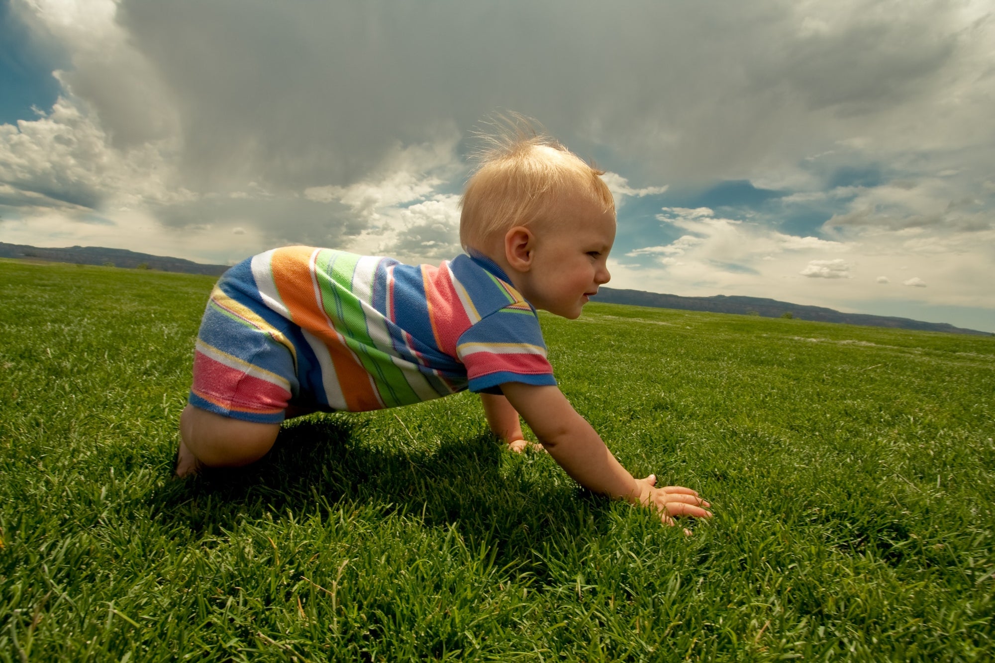 baby crawling on green grass with blue sky and clouds