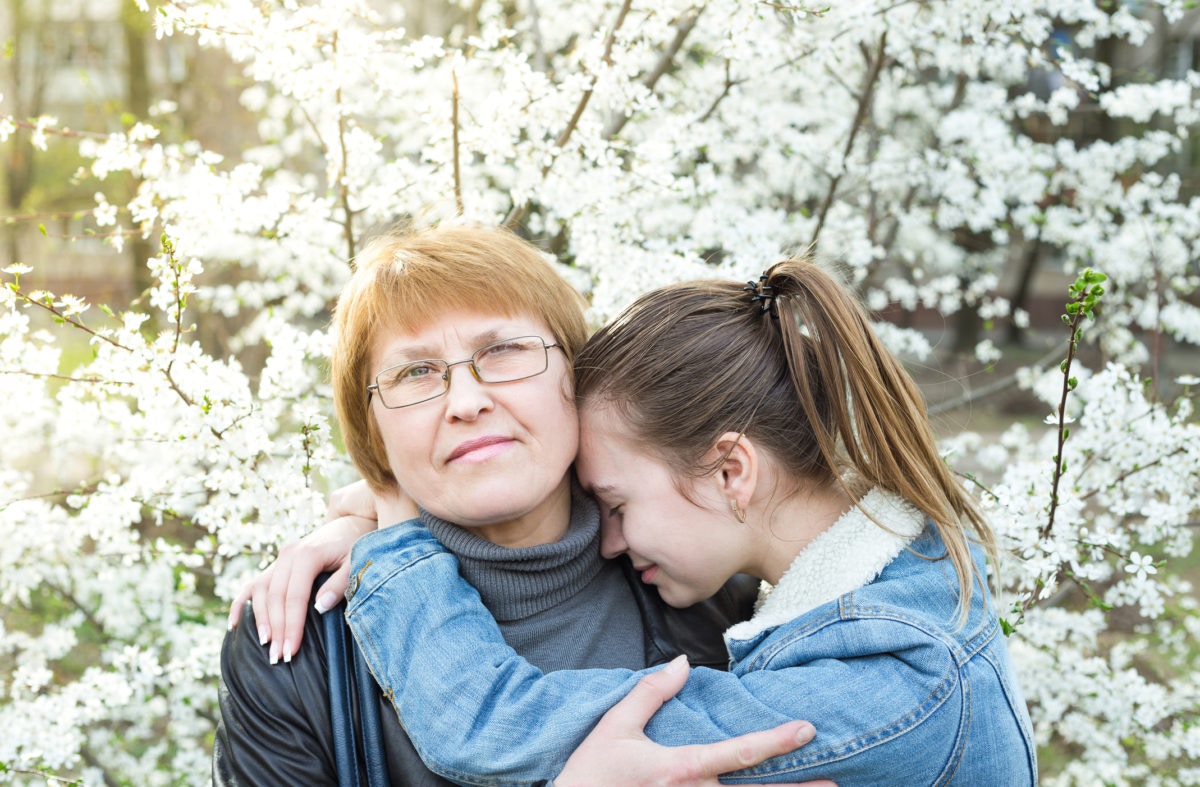 mother hugging her adult crying daughter on background of blooming trees