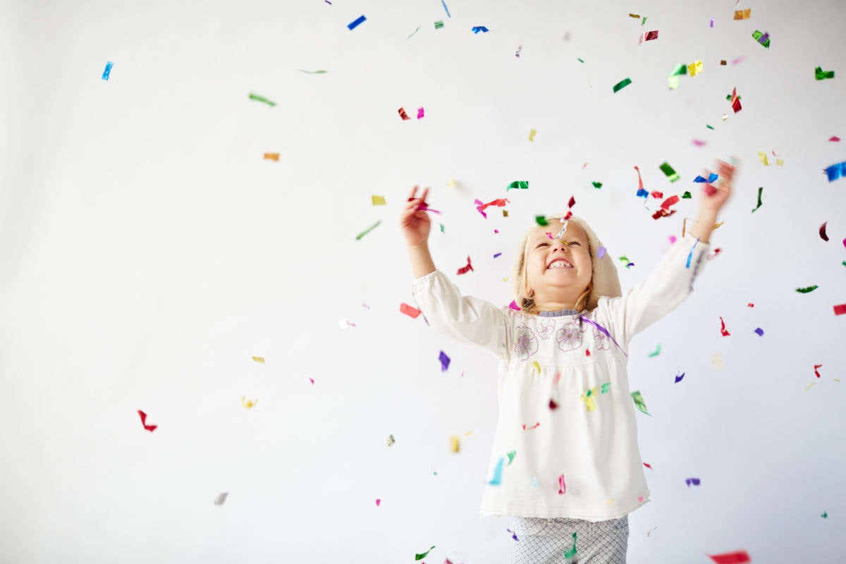 Happy little child girl with colorful confetti on white background
