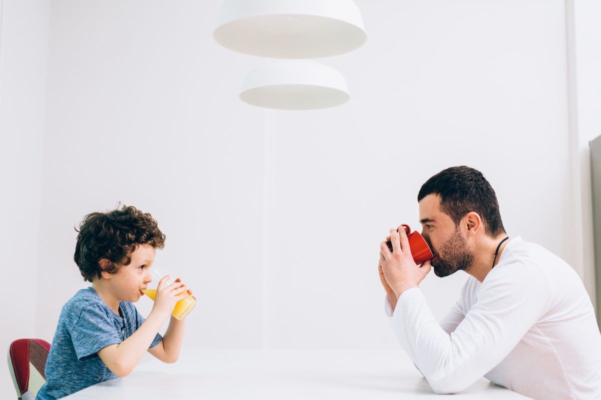 Father and son  drinking orange juice, sitting at dining table 