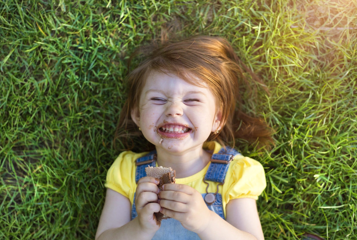 Little girl lying on the grass and eating chocolate